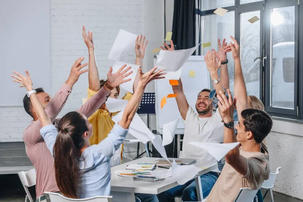 Zufriedene Geschäftsleute werfen bei Besprechung im Amt Dokumente weg — Stockfoto