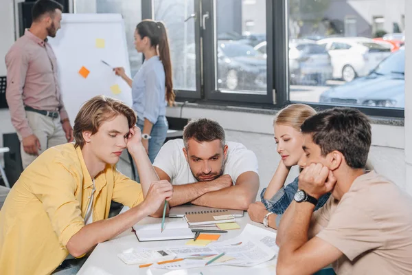 Empresarios cansados apoyados en la mesa durante la reunión en la oficina - foto de stock