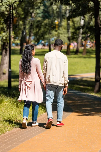 Rückansicht eines afrikanisch-amerikanischen Paares beim Händchenhalten und Gehen im Park — Stockfoto