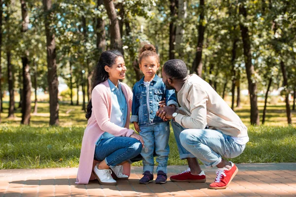 Genitori afro-americani accovacciati vicino figlia sul sentiero nel parco — Foto stock