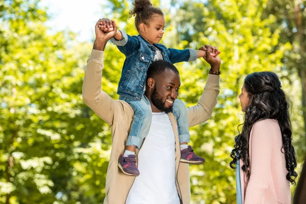 Sorridente padre afroamericano che tiene la figlia sulle spalle nel parco — Foto stock