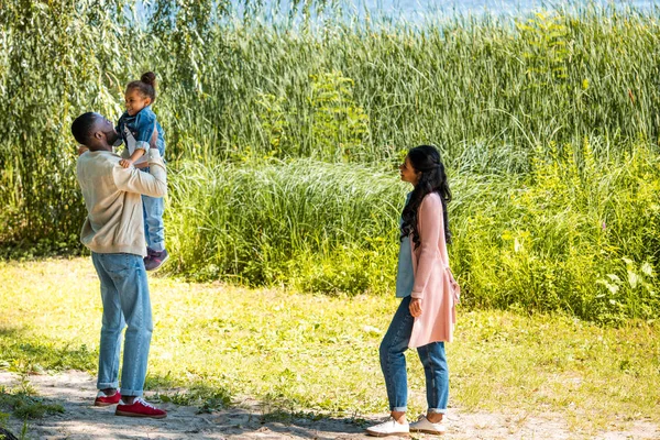 Père afro-américain tenant fille dans le parc près de la rivière — Photo de stock