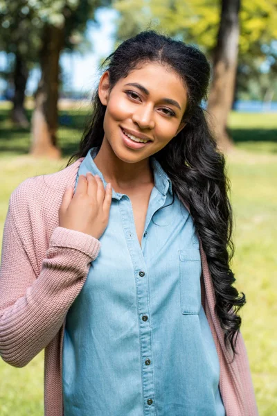 Sonriente atractiva afroamericana mujer posando en parque y mirando a la cámara - foto de stock