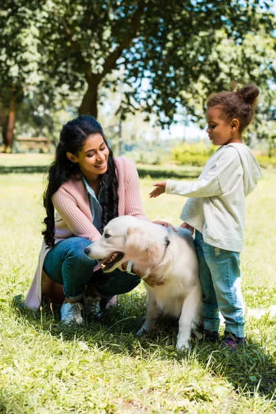 Smiling african american mother and daughter palming dog in park — Stock Photo