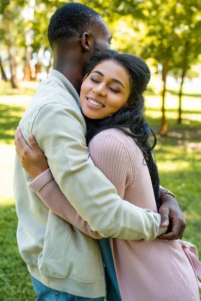 Vista lateral do casal afro-americano abraçando no parque — Fotografia de Stock