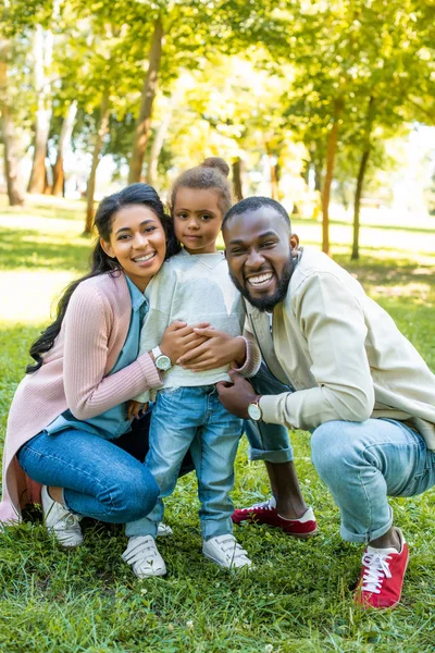 Sonrientes afroamericanos padres e hija mirando a la cámara en el parque - foto de stock