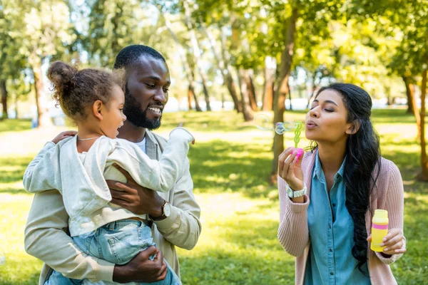 African american mother blowing soap bubbles in park — Stock Photo