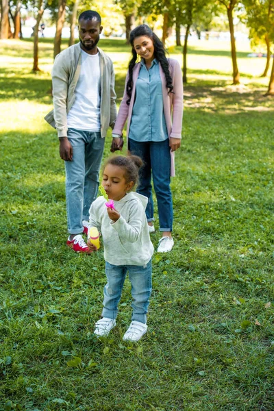 Afro americano figlia soffiando sapone bolle in parco — Foto stock
