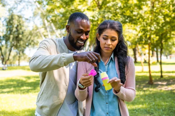 Africano americano coppia avendo divertimento con bottiglia per sapone bolle in parco — Foto stock