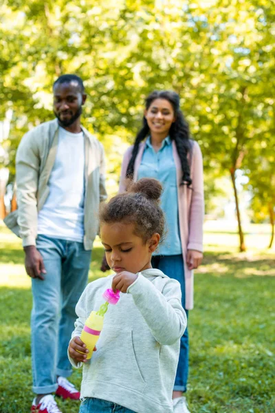 Afroamericano figlia in possesso di bottiglia per fare bolle di sapone nel parco — Foto stock