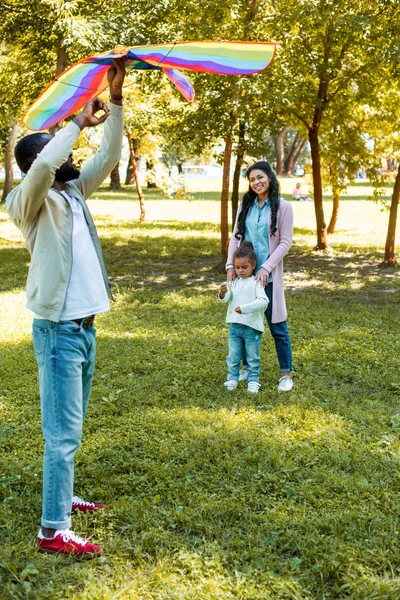 Afro-americano pai segurando arco-íris pipa acima da cabeça no parque — Fotografia de Stock