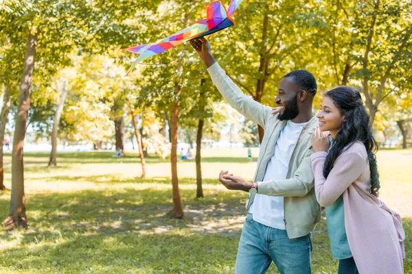 Vue latérale de heureux petit ami afro-américain tenant cerf-volant arc-en-ciel dans le parc — Photo de stock