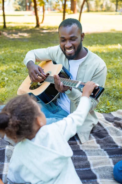 Афроамериканська дочка торкається гітари, а її батько грає в парку — стокове фото