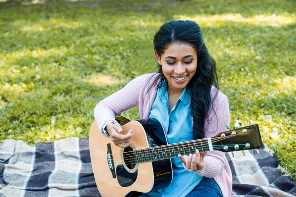 Attractive african american guitarist playing acoustic guitar in park — Stock Photo
