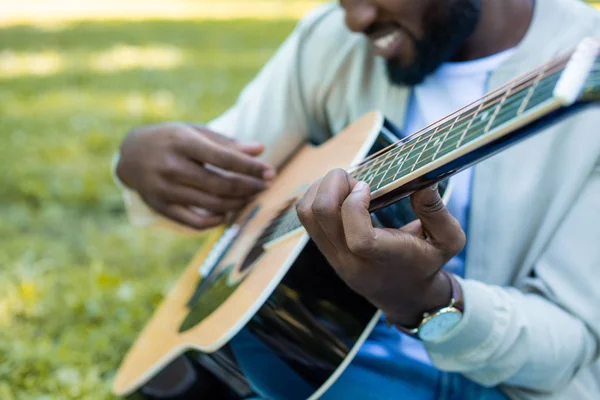 Imagen recortada del hombre afroamericano tocando la guitarra acústica en el parque - foto de stock