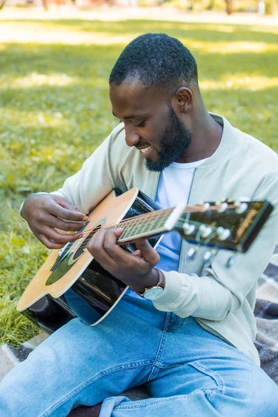 Smiling handsome african american man playing acoustic guitar in park — Stock Photo