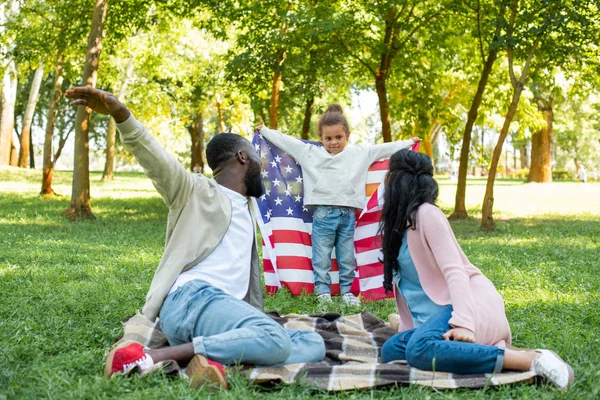 African american daughter pretending flying with american flag in park — Stock Photo