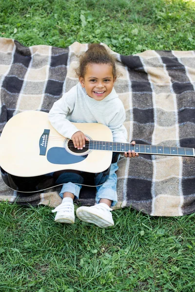 Vista ad alto angolo di sorridente adorabile bambino africano americano che tiene la chitarra acustica nel parco — Foto stock