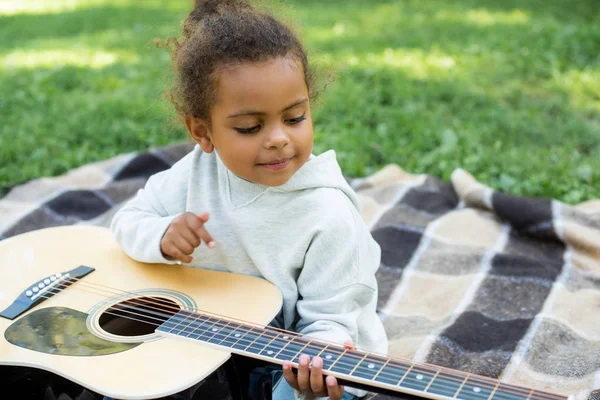 Adorabile ragazzo afroamericano che suona la chitarra acustica nel parco — Foto stock