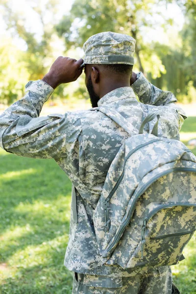 Back view of african american soldier in military uniform and bag wearing cap in park — Stock Photo