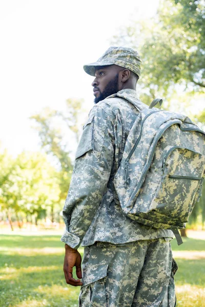 Visão de baixo ângulo do soldado afro-americano em uniforme militar e saco olhando para longe no parque — Fotografia de Stock