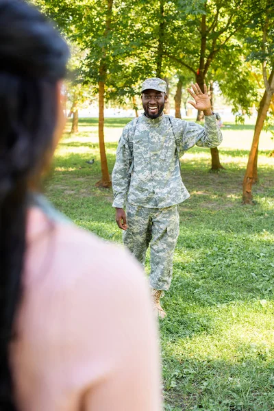 Imagen recortada de soldado afroamericano sonriente en uniforme militar saludando la mano a la novia en el parque - foto de stock