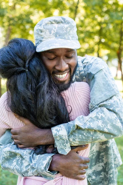Smiling african american soldier in military uniform cuddling girlfriend in park — Stock Photo