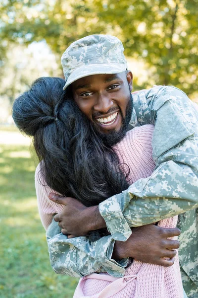 Heureux afro-américain soldat en uniforme militaire étreignant petite amie dans le parc — Photo de stock