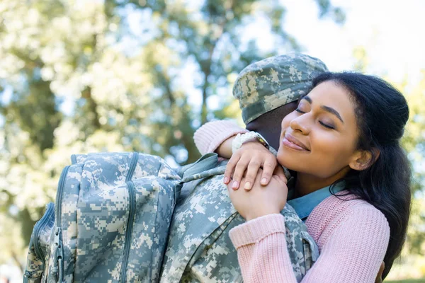 Soldado afroamericano en uniforme militar abrazando novia en parque - foto de stock