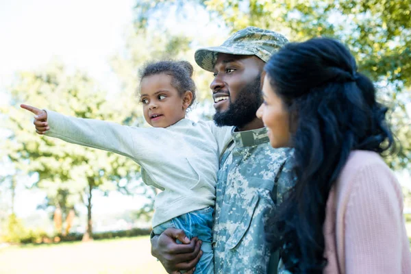 Afro-americana filha apontando em algo para o pai em uniforme militar e mãe no parque — Fotografia de Stock