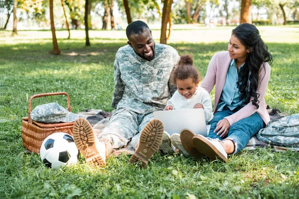 Afrikanischer amerikanischer Soldat in Militäruniform sieht aus, wie Tochter Laptop im Park benutzt — Stockfoto