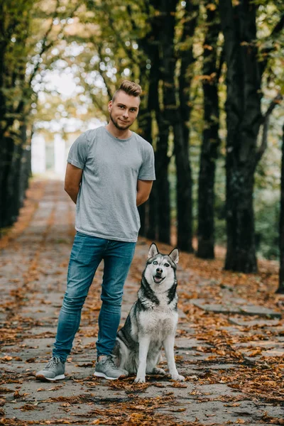 Giovane con cane husky siberiano nel parco autunnale — Foto stock