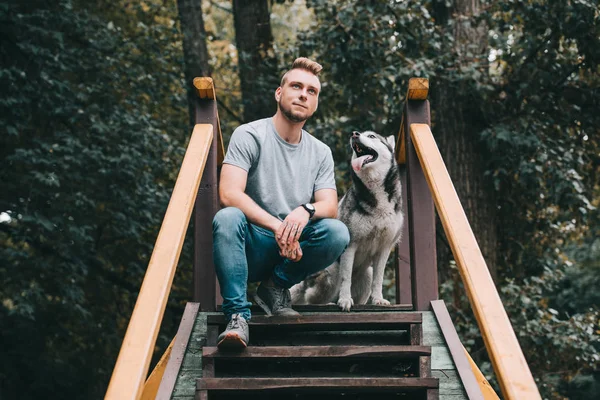 Jeune homme assis sur les escaliers avec chien husky sibérien — Photo de stock