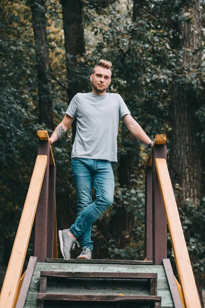 Hombre guapo posando en escaleras en el parque y mirando a la cámara - foto de stock