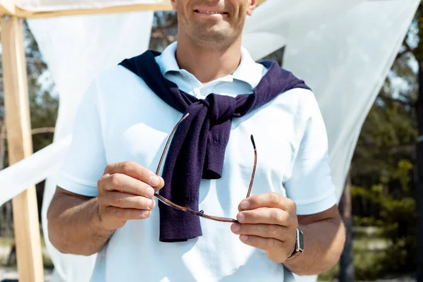 Cropped shot of man holding eyeglasses in hands with white curtain lace on background — Stock Photo