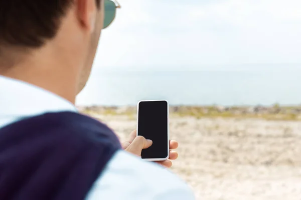 Partial view of man using smartphone with blank screen on sandy beach — Stock Photo