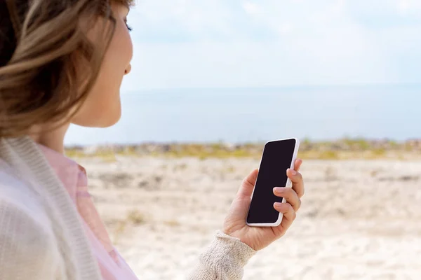 Partial view of woman using smartphone with blank screen on sandy beach — Stock Photo