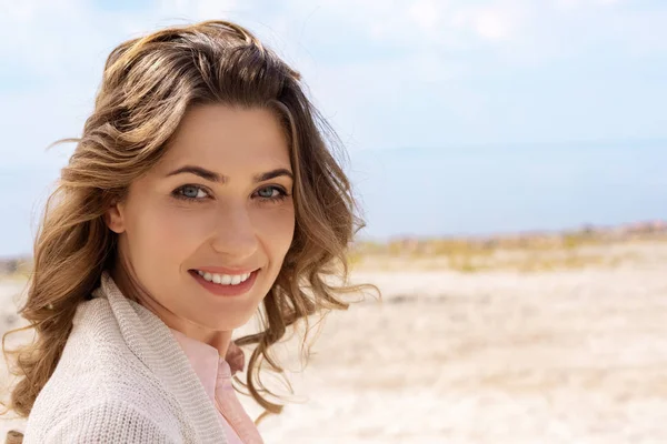 Retrato de la mujer sonriente mirando a la cámara en la playa de arena - foto de stock