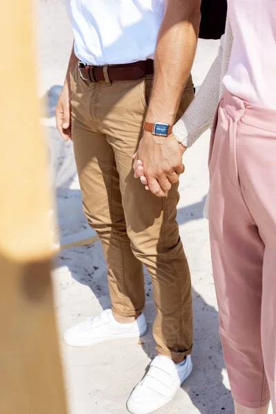Vista parcial de la pareja cogida de la mano mientras camina por la playa de arena - foto de stock