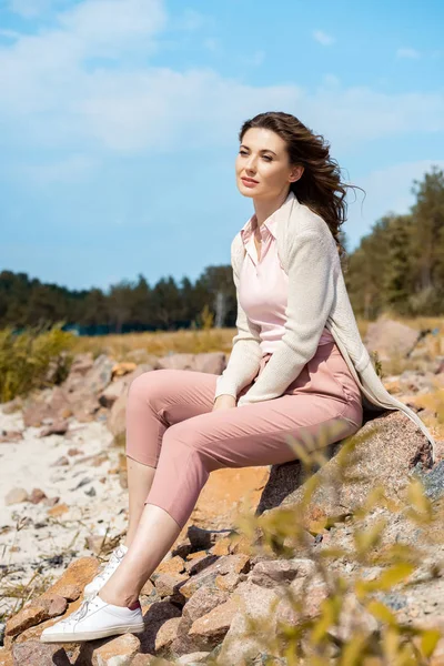 Attraente donna pensierosa poggiata su rocce sulla spiaggia di sabbia — Foto stock