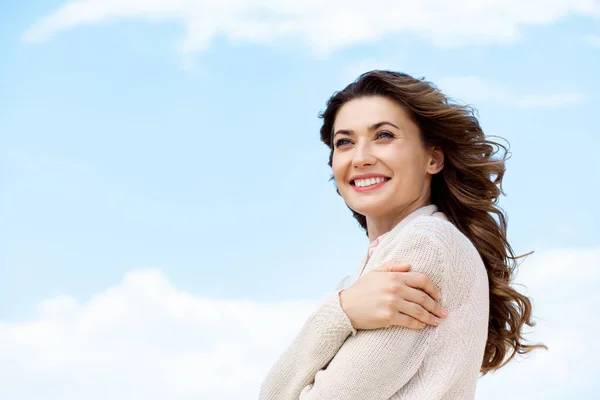 Vista lateral de la hermosa mujer sonriente con el cielo azul nublado en el fondo - foto de stock