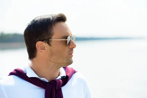 Seitenansicht eines gutaussehenden Mannes mit Sonnenbrille, der mit Fluss im Hintergrund wegschaut — Stockfoto