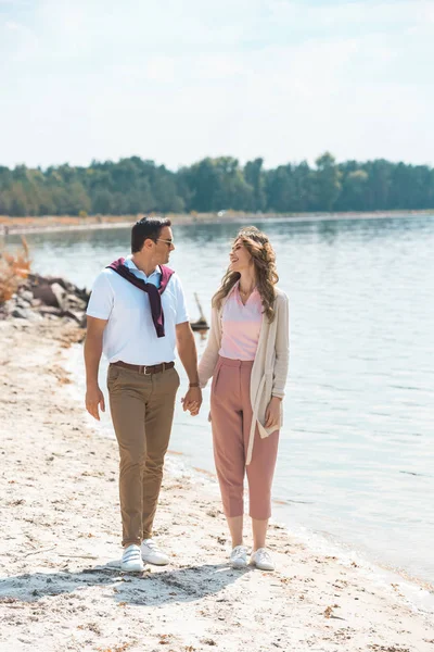Romantic couple holding hands while walking on sandy riverside — Stock Photo