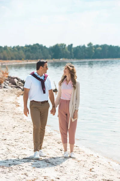 Couple romantique tenant la main tout en marchant sur le bord de la rivière de sable — Photo de stock