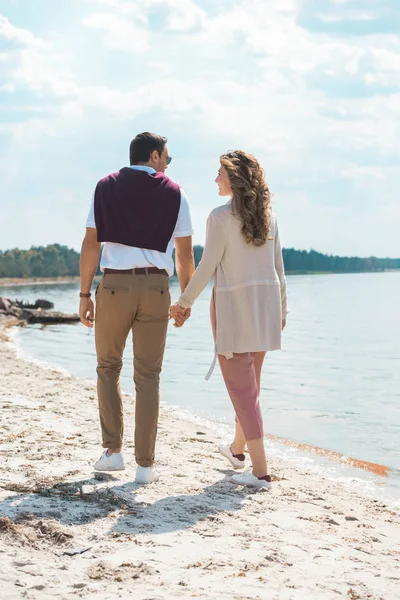 Couple romantique tenant la main tout en marchant sur le bord de la rivière de sable — Photo de stock
