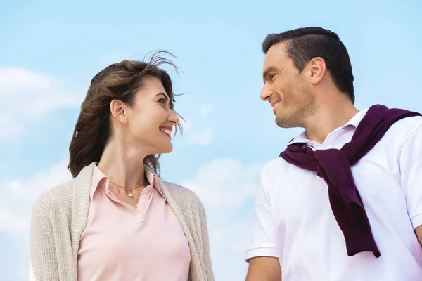 Retrato de pareja sonriente mirándose con el cielo azul en el fondo - foto de stock