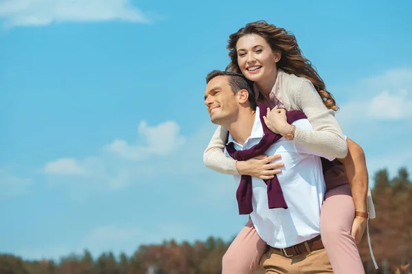 Cheerful couple piggybacking together with blue cloudy sky on background — Stock Photo