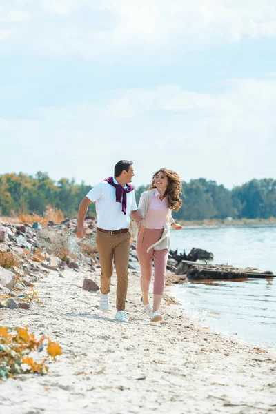 Feliz pareja cogida de la mano mientras se ejecuta en la playa de arena - foto de stock