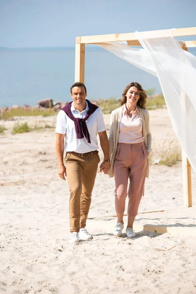 Happy couple holding hands while walking on sandy beach — Stock Photo