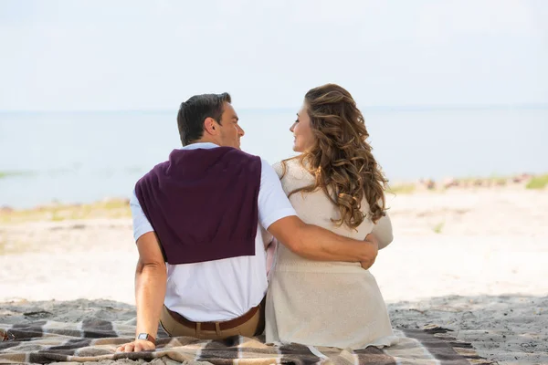 Vue arrière du couple romantique reposant sur une couverture sur une plage de sable — Photo de stock